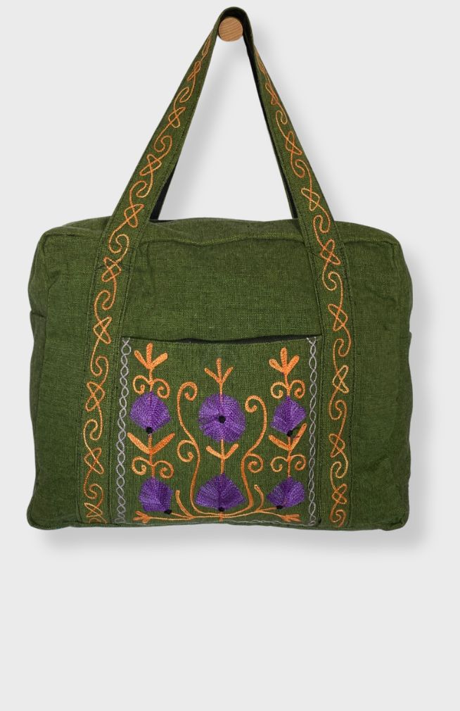 A heavy cotton duffel bag featuring front and back pockets with detailed floral embroidery, handmade in Nepal.