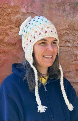 Winter wool earflap hat with top and side tassels.  White with rainbow-colored tic tic design