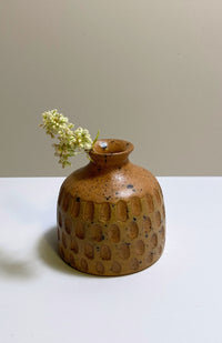 A small round ceramic bud vase with a textured surface and speckled brown and tan glaze, handmade in Nepal.