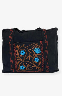 A heavy cotton duffel bag featuring front and back pockets with detailed floral embroidery, handmade in Nepal.