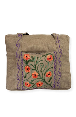 A heavy cotton duffel bag featuring front and back pockets with detailed floral embroidery, handmade in Nepal.