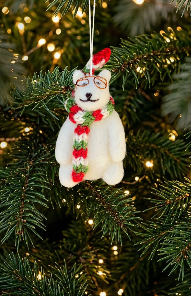 A white felted wool polar bear ornament with glasses and a red, green, and white striped scarf. Handmade in Nepal.
