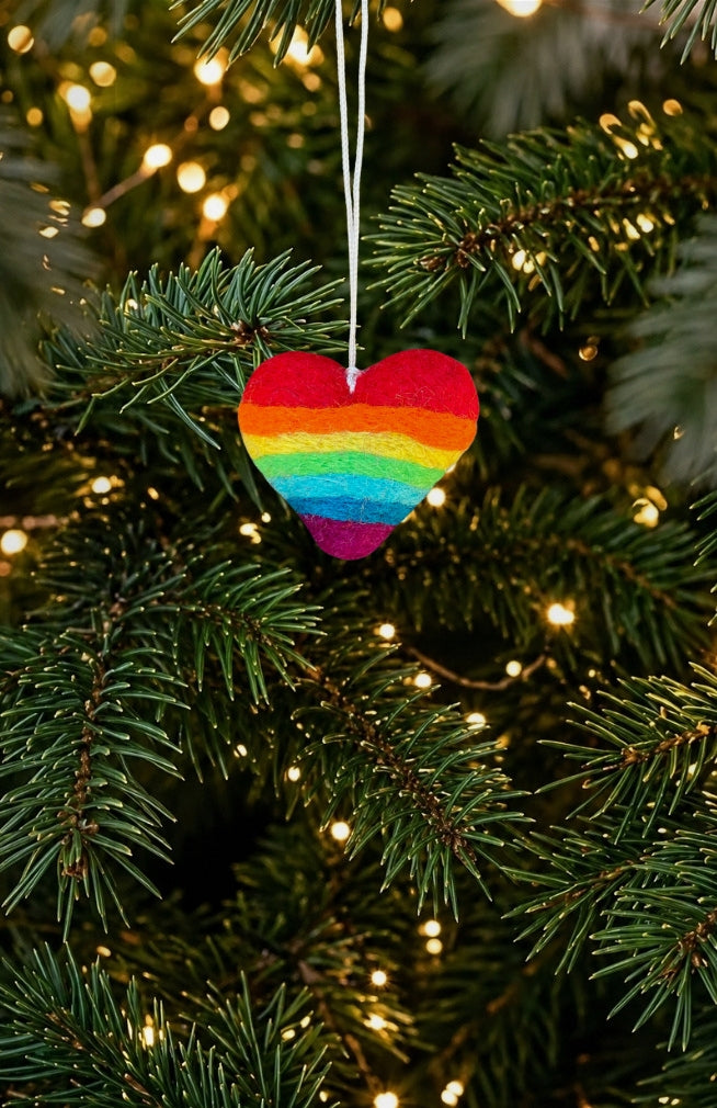 A heart-shaped felt Christmas ornament with a rainbow stripe pattern. Handmade in Nepal.