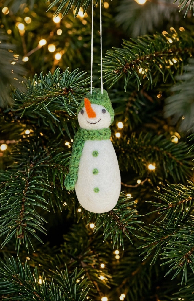 A felt snowman Christmas ornament with a green hat and scarf, orange carrot nose, and green buttons, handmade in Nepal.