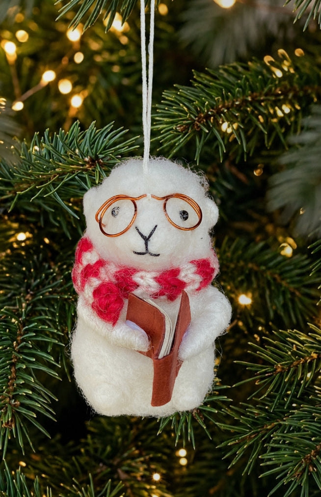 A white felted sheep ornament reading a book with round glasses and red-and-white patterned scarf.