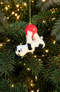 A black and white cat hanging from a ball Christmas ornament, handmade in Nepal with 100% New Zealand wool.