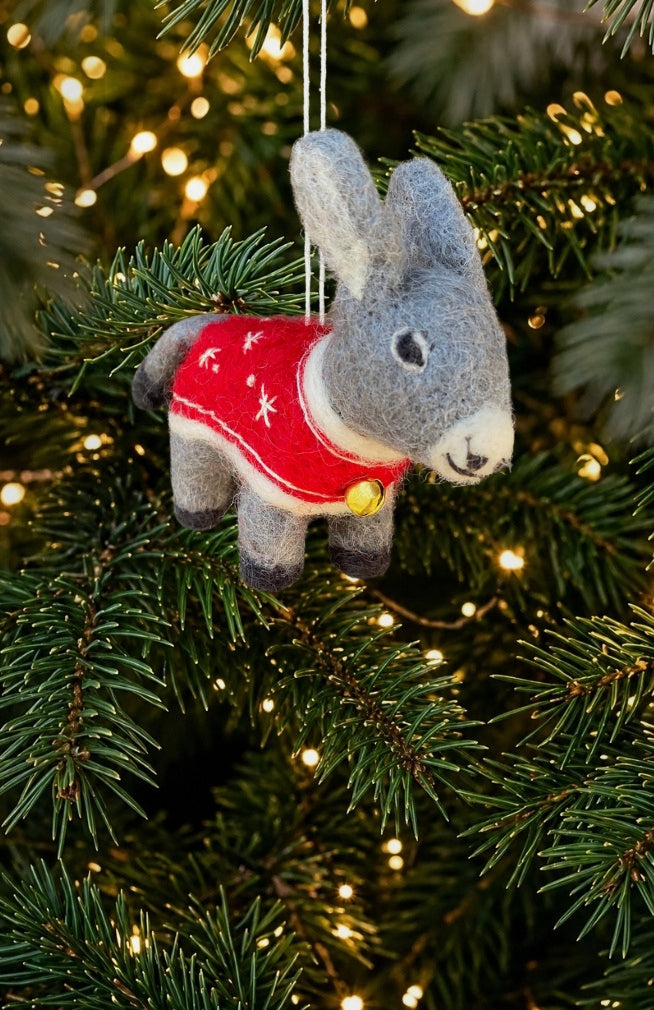 A hand felted wool donkey Christmas ornament wearing a red sweater with white stars and a gold bell.