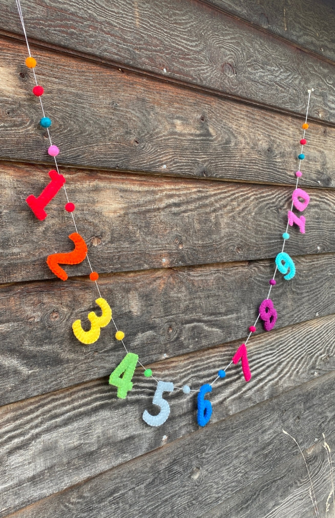 A handmade colorful number garland with colorful felt balls between numbers spelling out 1 -10 .