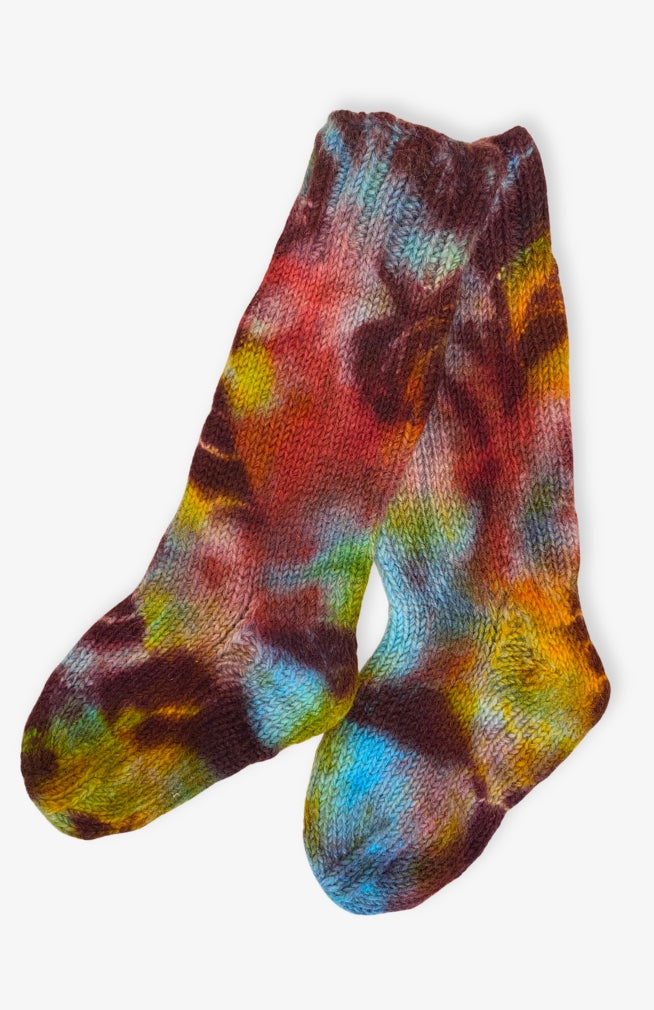 A pair of hand-knit socks featuring a vibrant tie-dye pattern with blue, purple, green, yellow, and red tones. Handmade by artisans in Nepal.