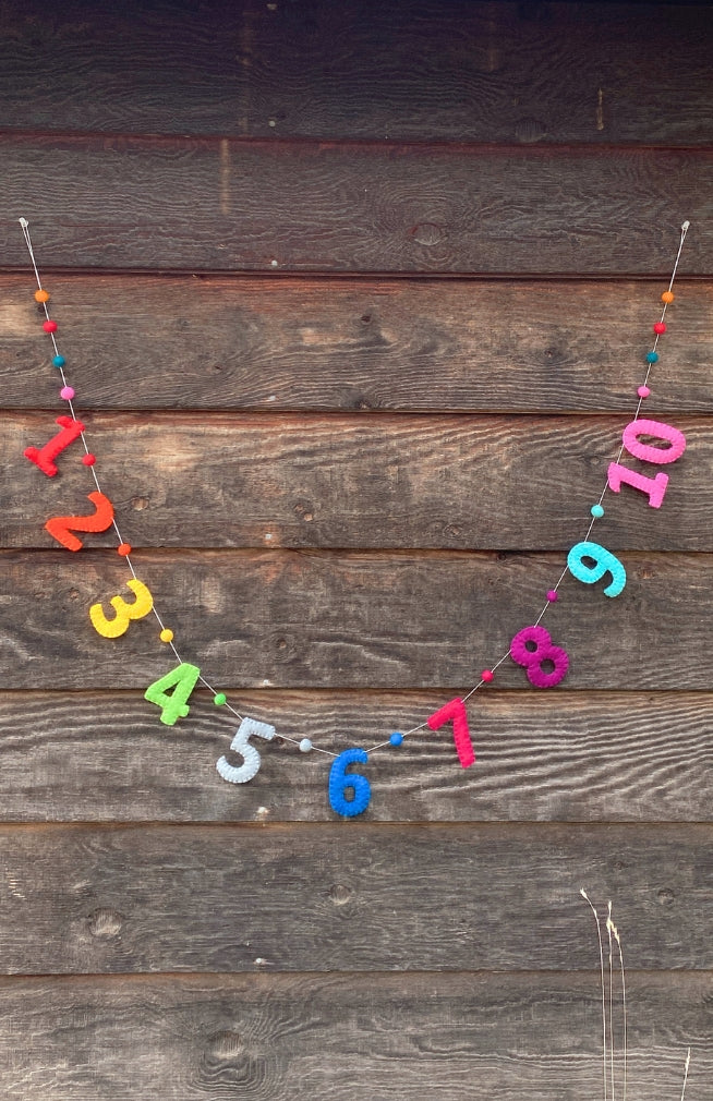 A handmade colorful number garland with colorful felt balls between numbers spelling out 1 -10 