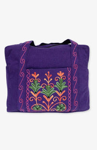 A heavy cotton duffel bag featuring front and back pockets with detailed floral embroidery, handmade in Nepal.